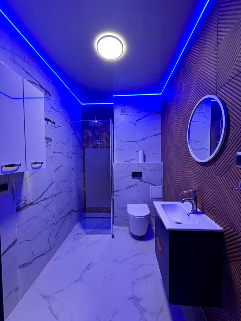 Nowoczesna łazienka z prysznicem walk-in i nastrojowym oświetleniem LED w kolorze niebieskim.