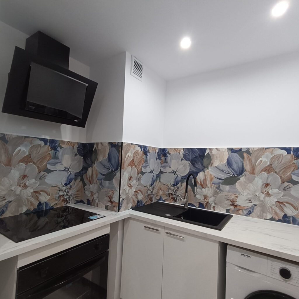 Kuchnia po generalnym remoncie z czarnym zlewem, białymi szafkami i dekoracyjnym panelem ściennym.