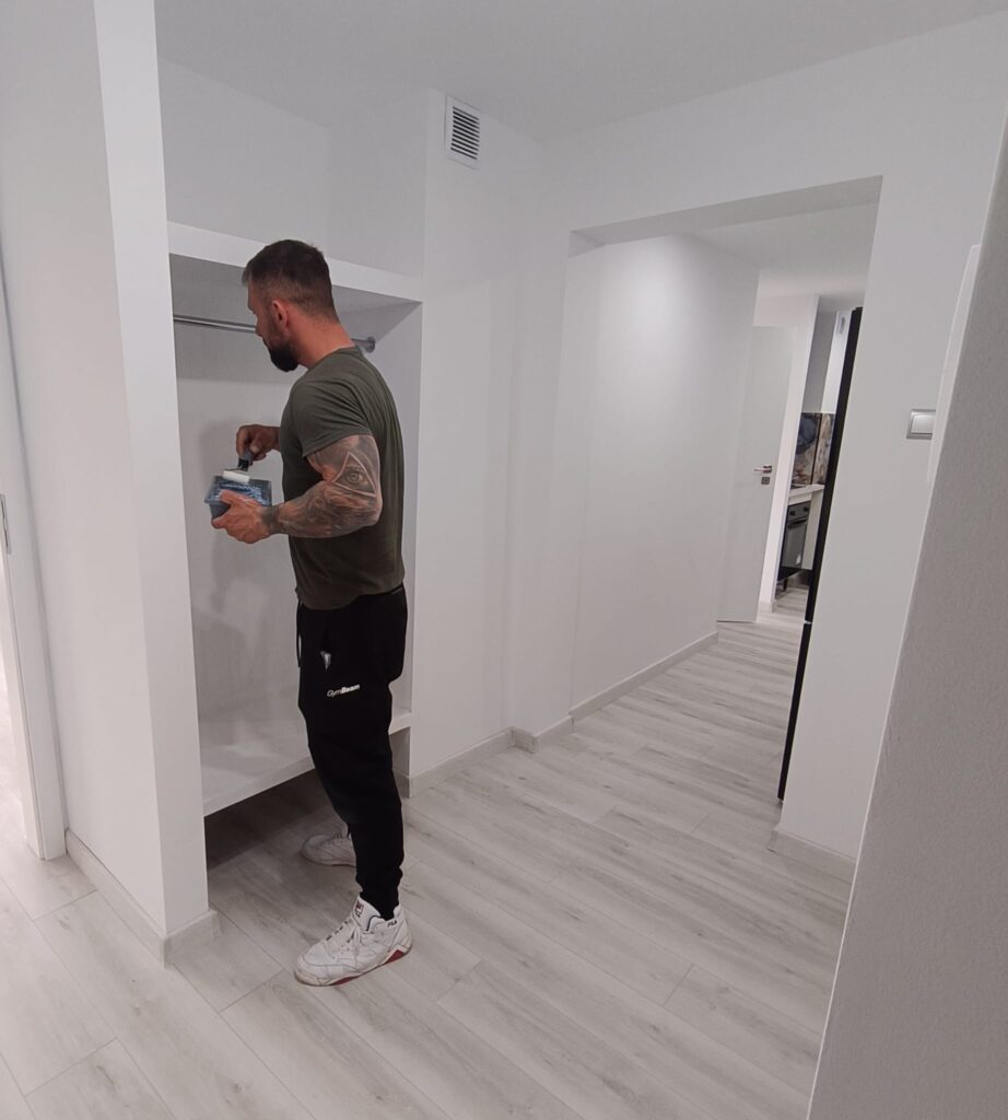 Pracownik podczas prac wykończeniowych w przedpokoju mieszkania po remoncie, jasne ściany i podłoga winylowa.