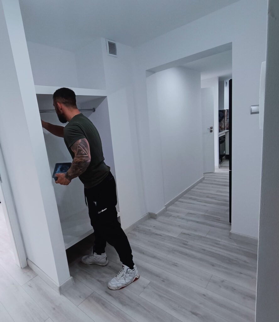 Prace wykończeniowe w korytarzu mieszkania, montaż elementów zabudowy w jasnym wnętrzu.