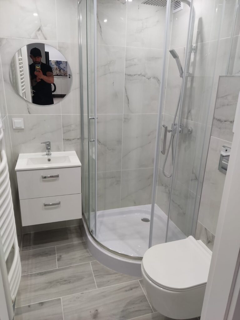 Łazienka po remoncie z kabiną prysznicową, jasnymi płytkami imitującymi marmur i podwieszaną toaletą.